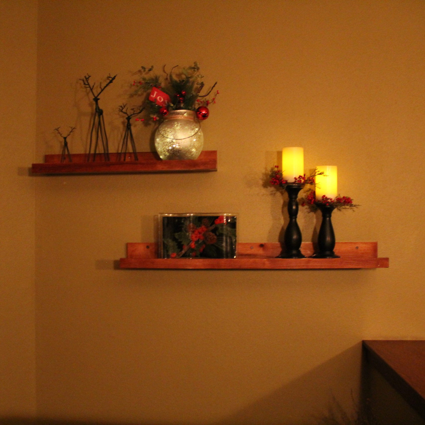 My Dave built floating shelves in the entry way are fun to decorate. I love the wrought iron reindeer, the frosted glass lantern filled with mini LEDs on an automatic timer and topped with greenery. The Peggy Karr holiday plate and candles collared in berries complete the display.