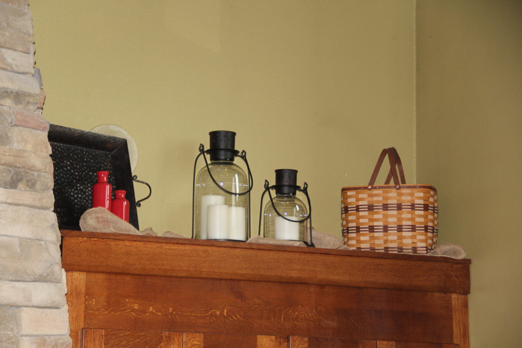 Cabinets up top with lanterns, some burlap, a bronze tray with red vases and a Longaberger basket.