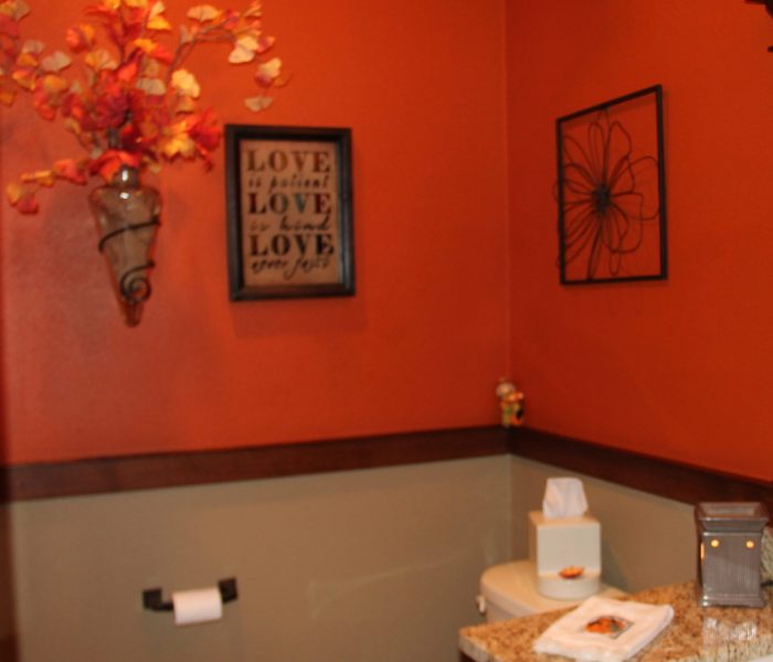 The powder room from another angle. I divided the walls in this smaller space with a chair rail and painted it two different colors. The burnt orange is fun for all seasons. Adding different textures when decorating  is important. Here the glass, the burlap, the wrought iron and florals all stand out.